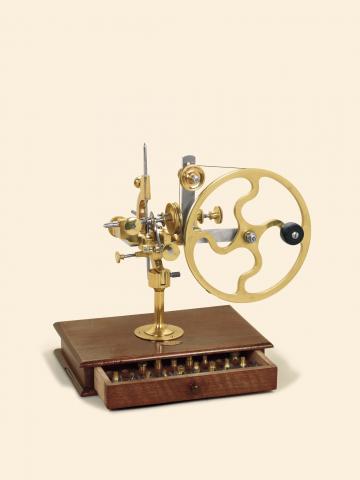 Sandoz Fils & Co., La Chaux-de-Fonds & Bienne, circa 1890. Fine brass and steel rounding up tool. Large crank lever wheel, horizontal depth slide controlled by a knurled nut, two stop posts, wooden base with a drawer for additional cutters and cutter chuc